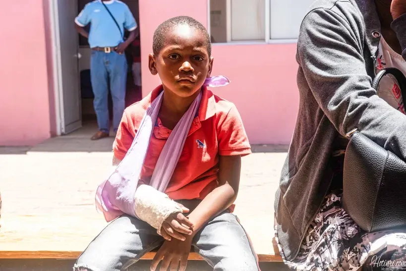 A young boy with a cast on his arm is sitting on a bench.