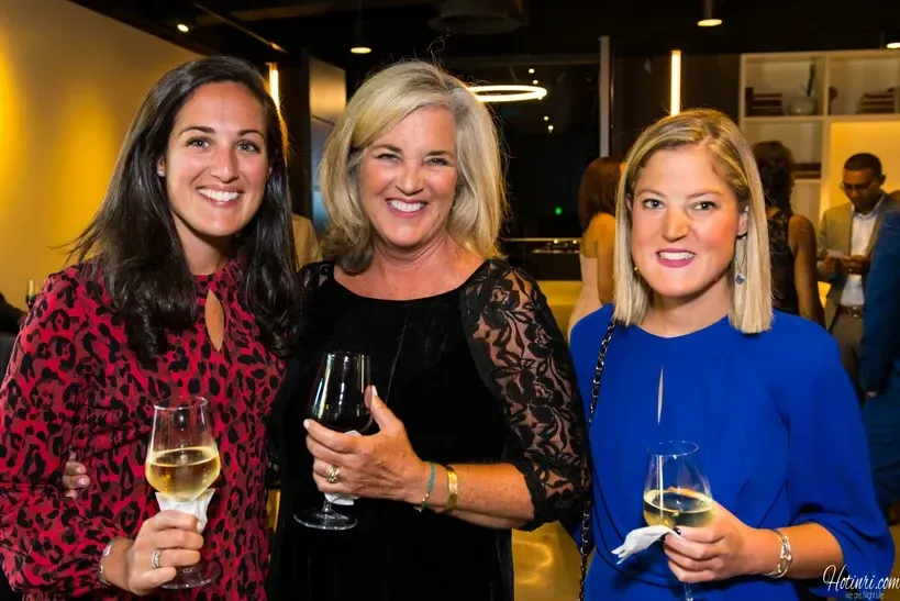 Three women are standing next to each other holding wine glasses.