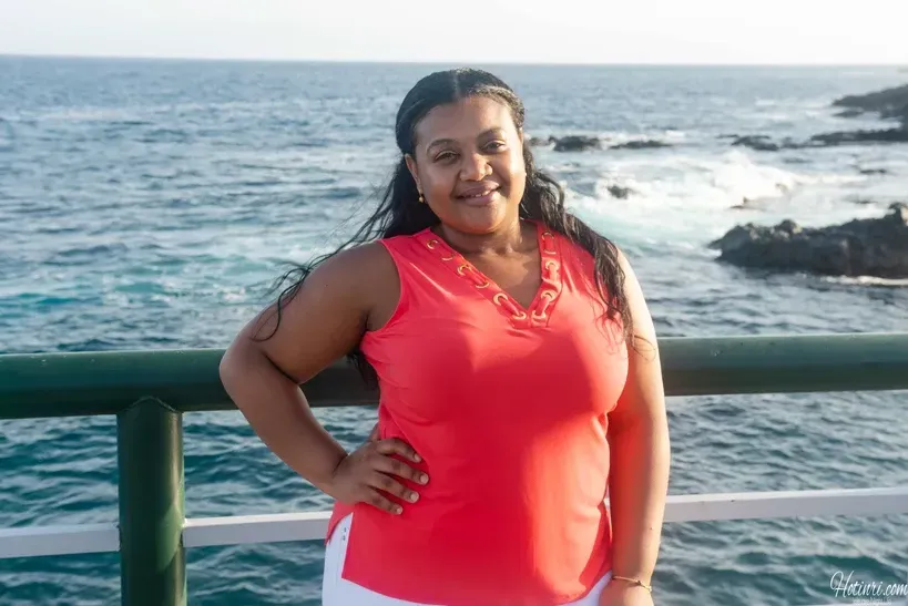 A woman in a pink tank top is standing on a pier overlooking the ocean.