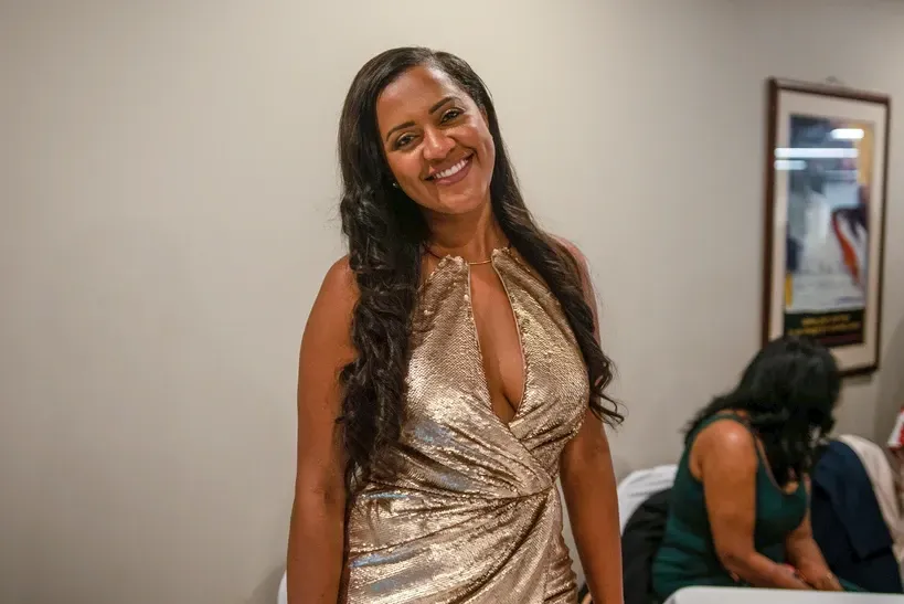 A woman in a gold dress is smiling in a room.