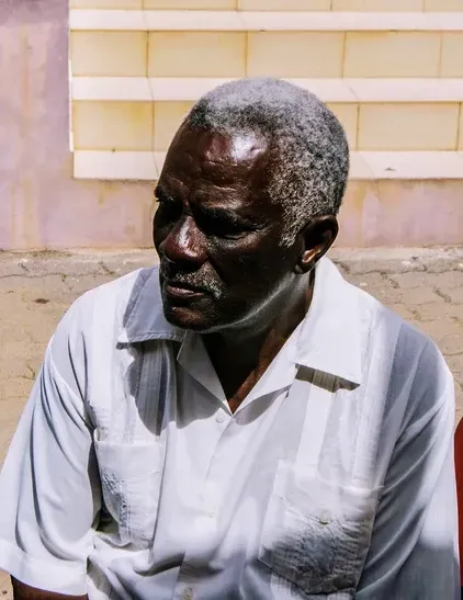 A man with gray hair and a beard is wearing a white shirt