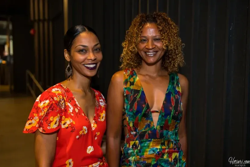 Two women are posing for a picture together in front of a black wall.