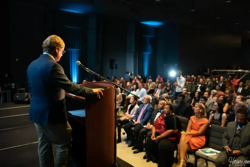 A man is giving a speech at a podium in front of a crowd.