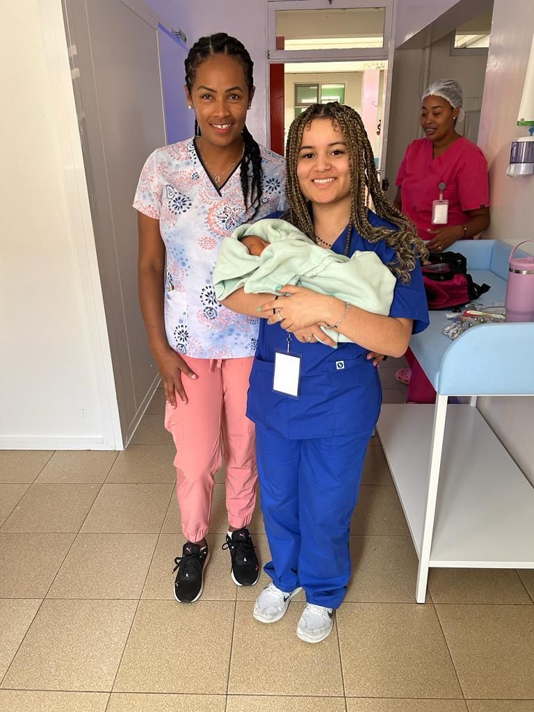 Two nurses are standing next to each other holding a baby in a hospital.