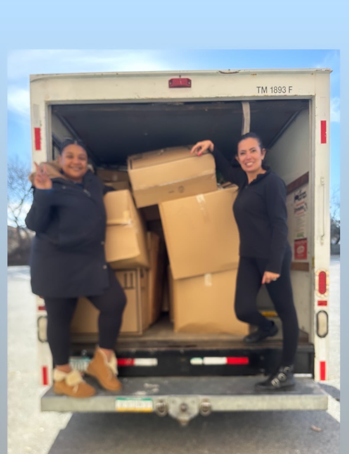 Two women are standing in the back of a truck filled with cardboard boxes