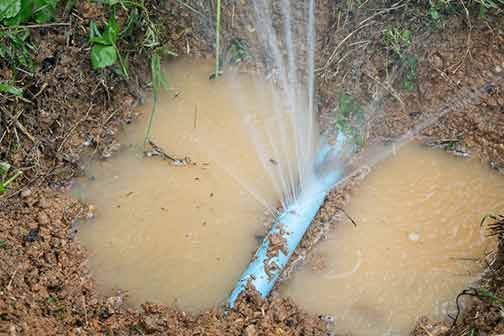 A water pipe is leaking water into a puddle in the dirt.
