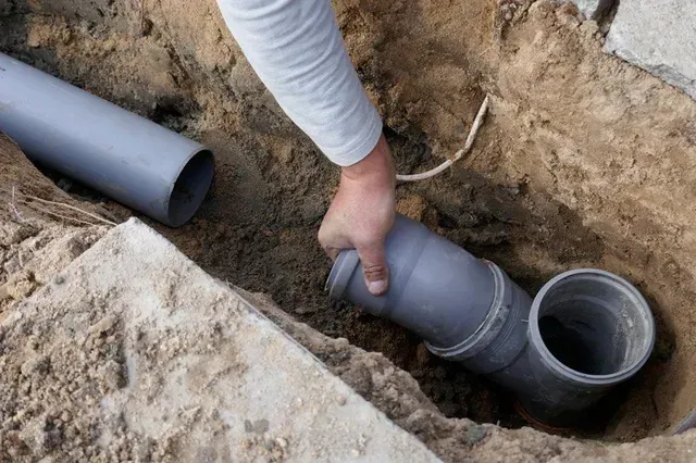 A person is holding a pipe in a hole in the ground.