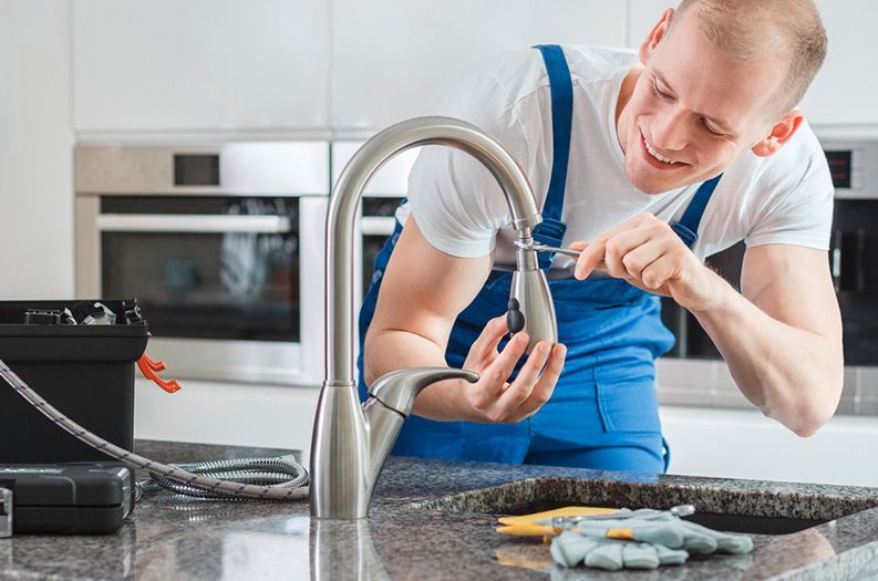 A plumber is fixing a faucet in a kitchen.