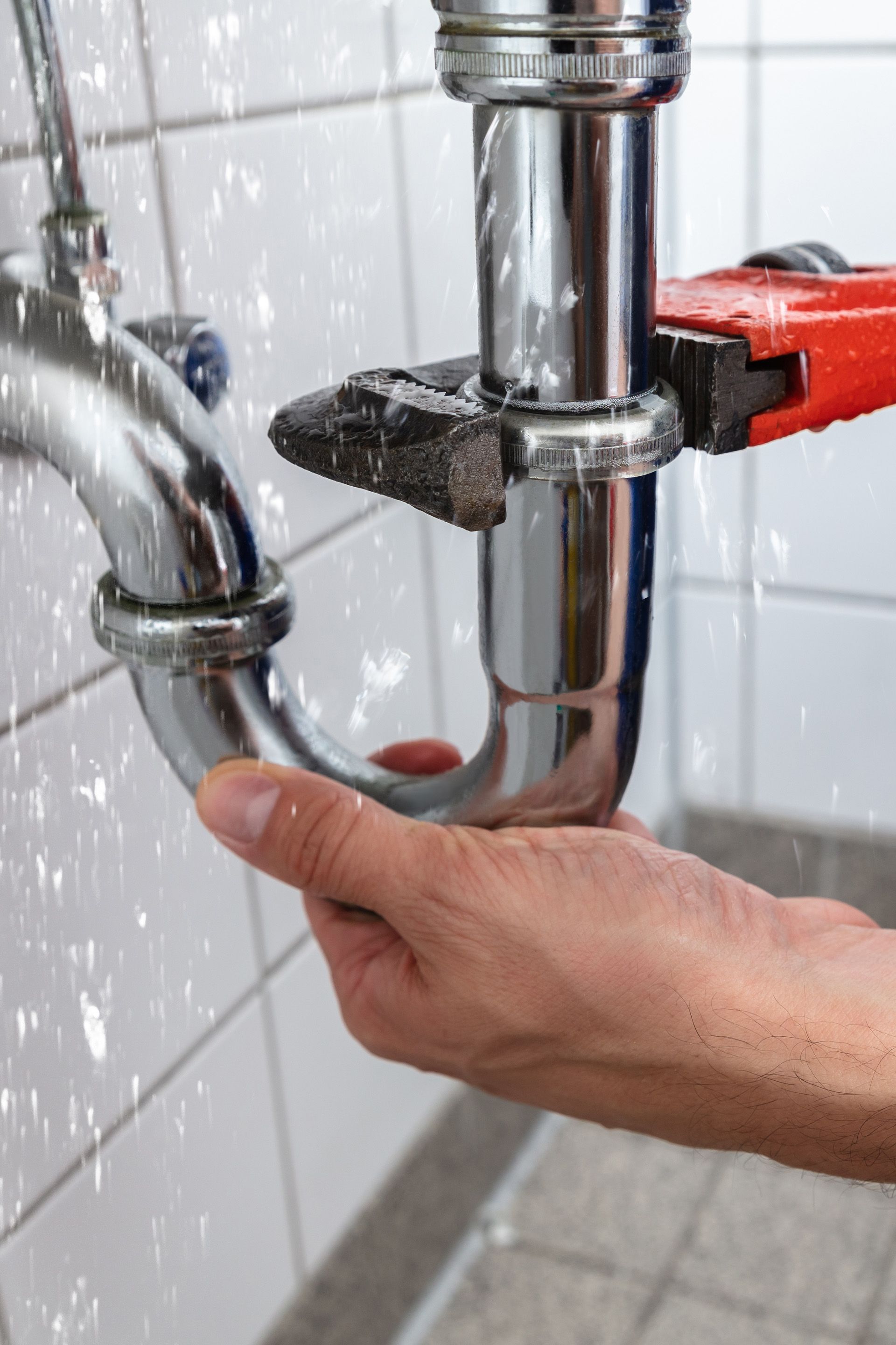 A person is fixing a sink pipe with a wrench.