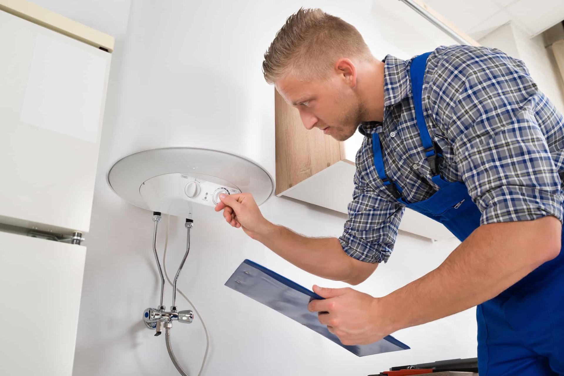 A man is looking at a water heater while holding a clipboard.