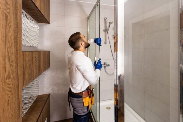 A man is installing a shower door in a bathroom.