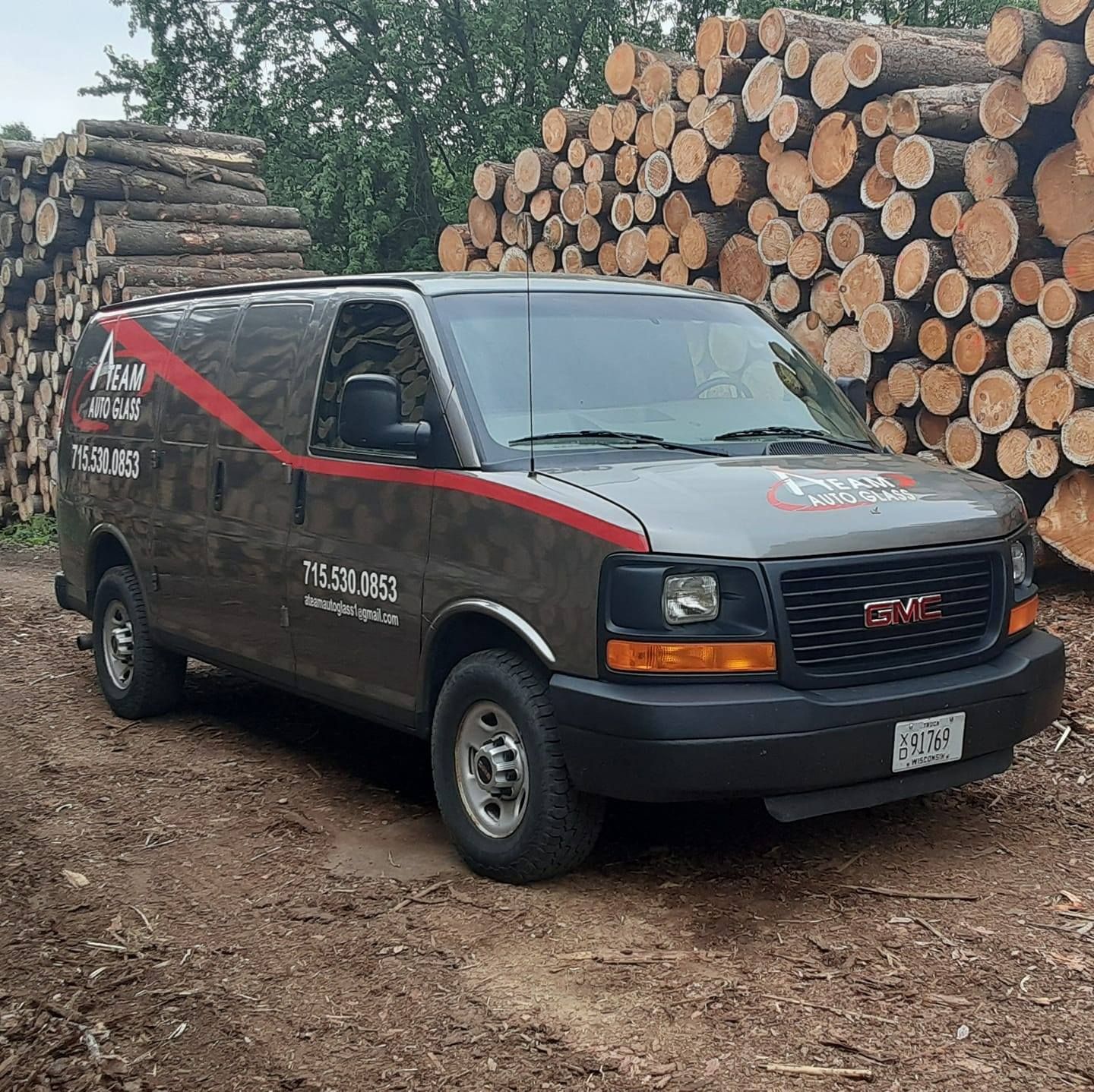A gmc van is parked in front of a pile of logs.