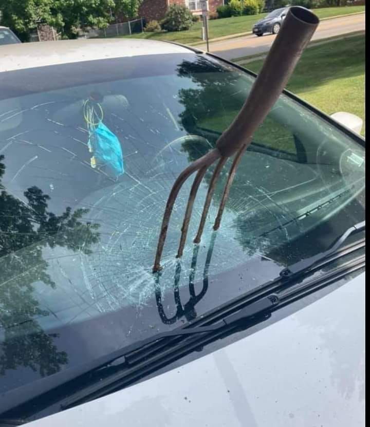 A fork is sticking out of the windshield of a car.