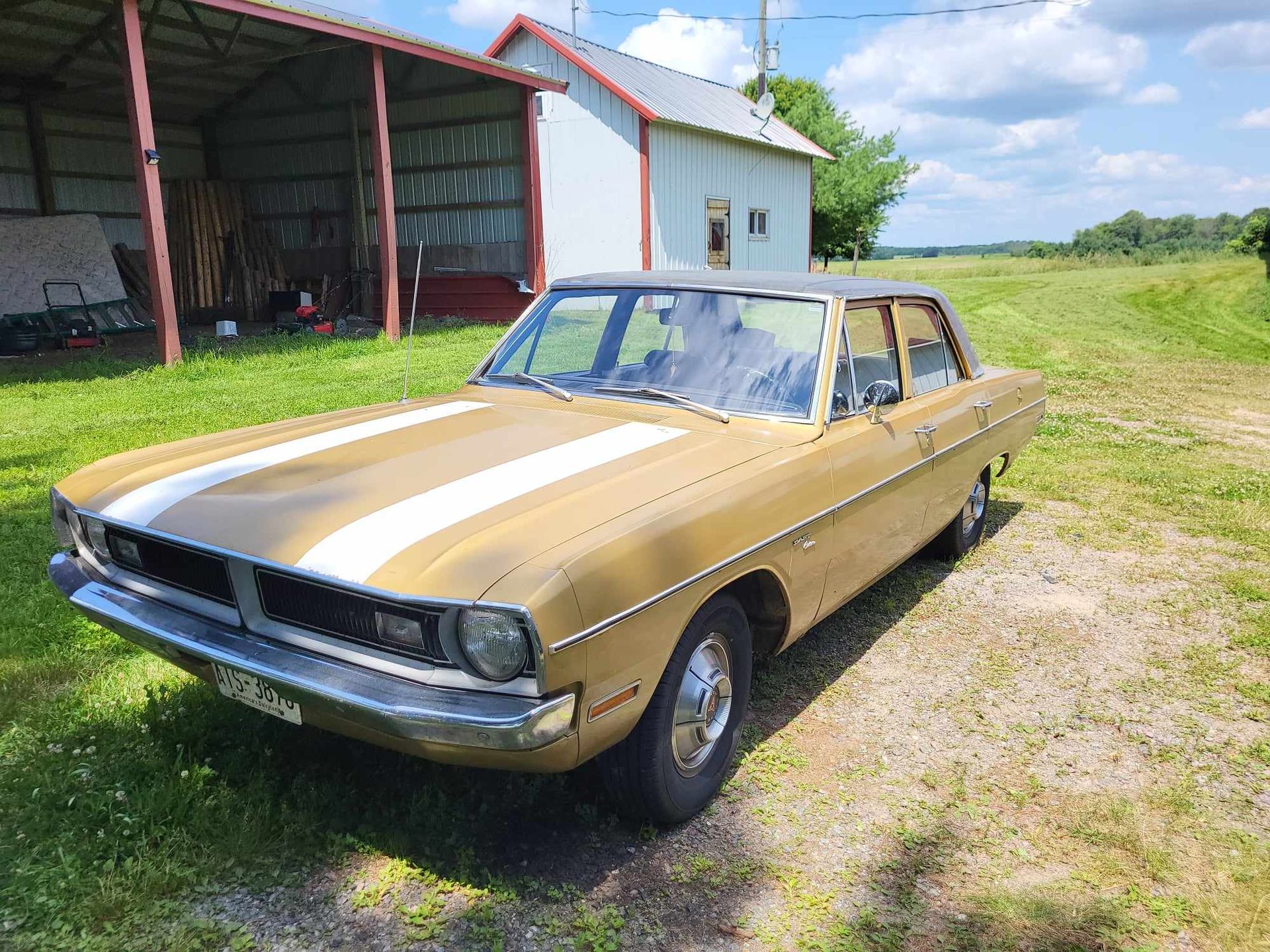 A gold car with white stripes on the side is parked in a grassy field.