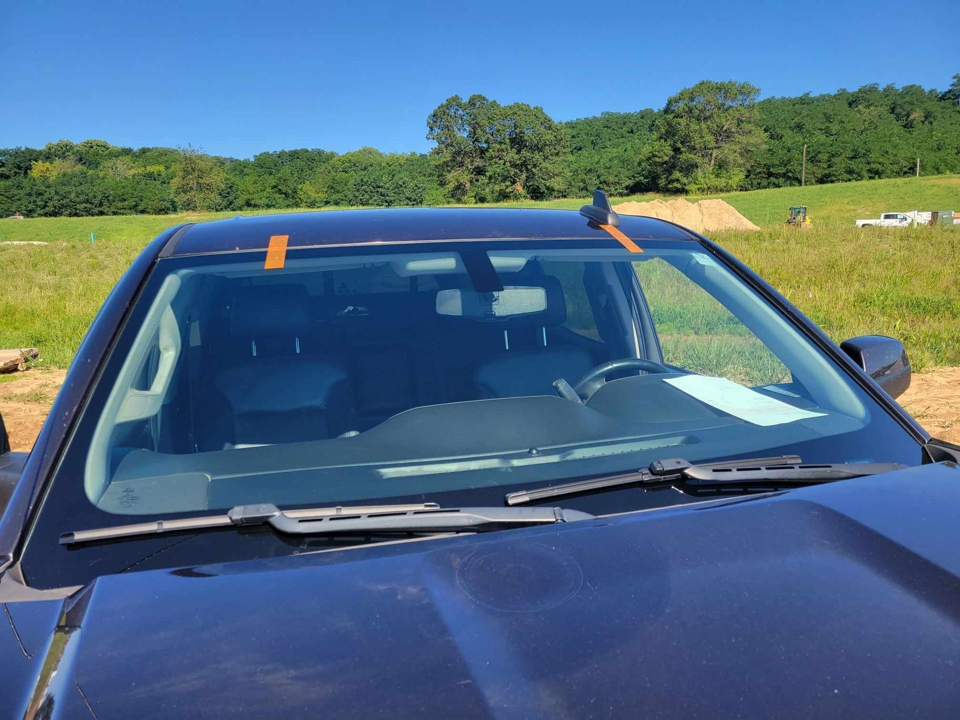 A black car with a windshield sticker on it is parked in a field.