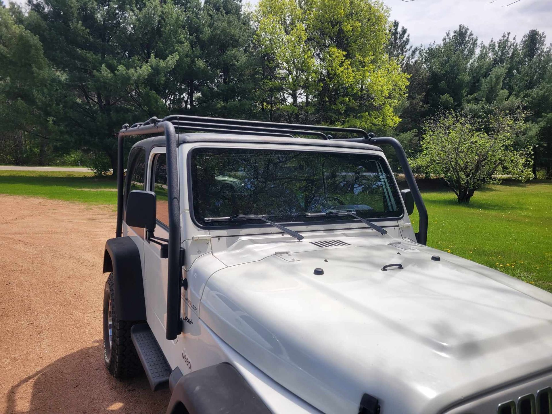 A white jeep with a roof rack is parked on a dirt road.