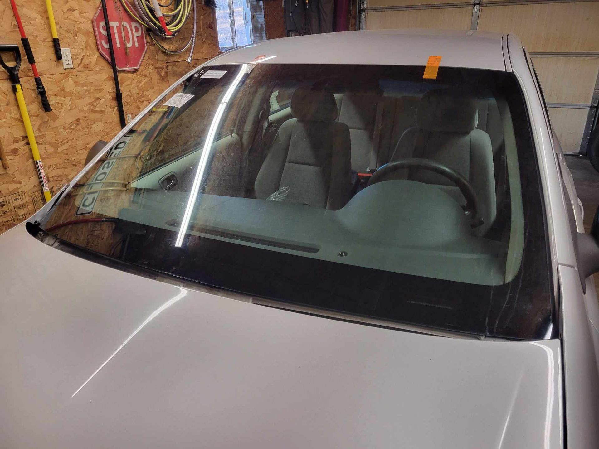 A silver car with a new windshield is parked in a garage.