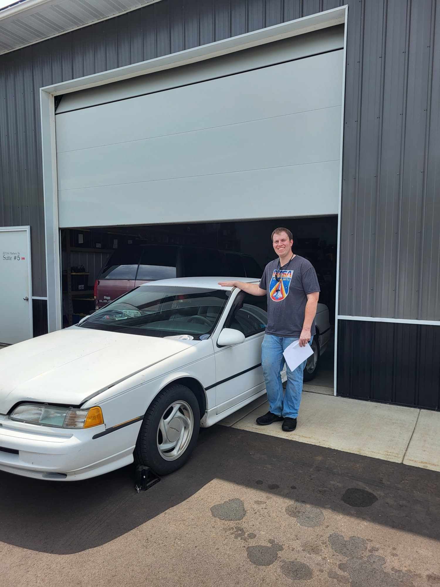 A man is standing next to a white car in front of a garage door.