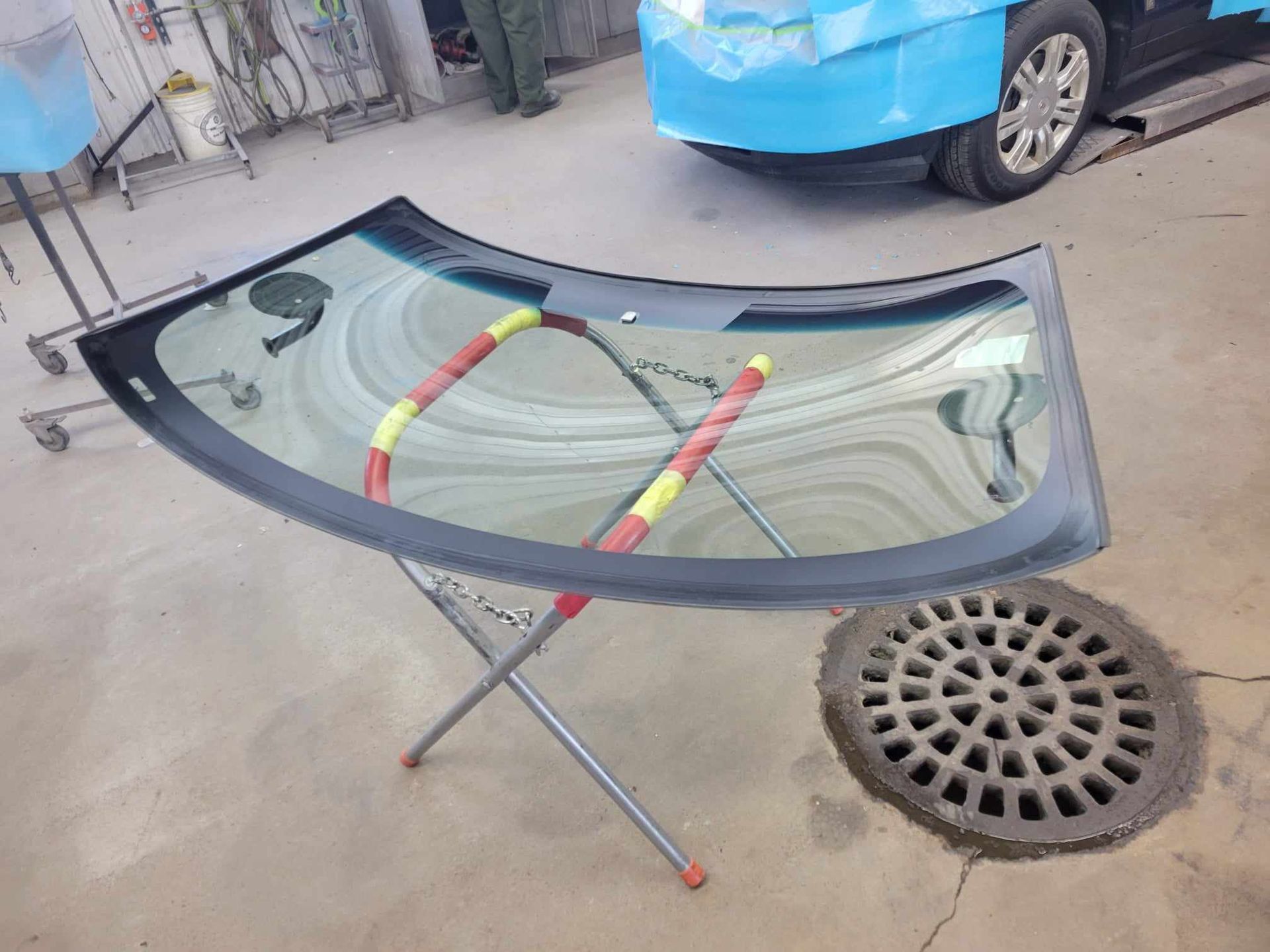 A windshield is sitting on a stand next to a manhole cover.