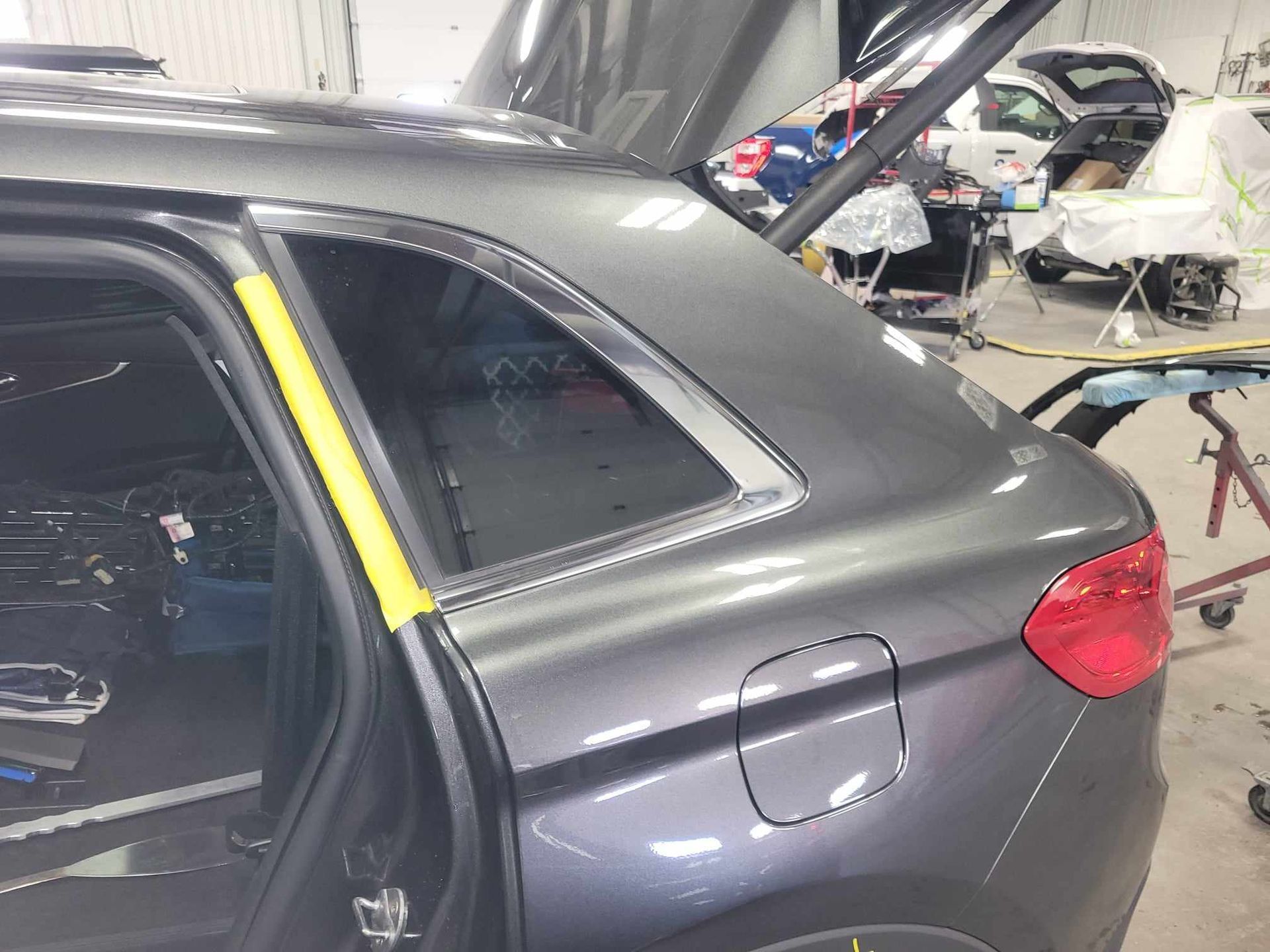 A car is being worked on in a garage with the trunk open.