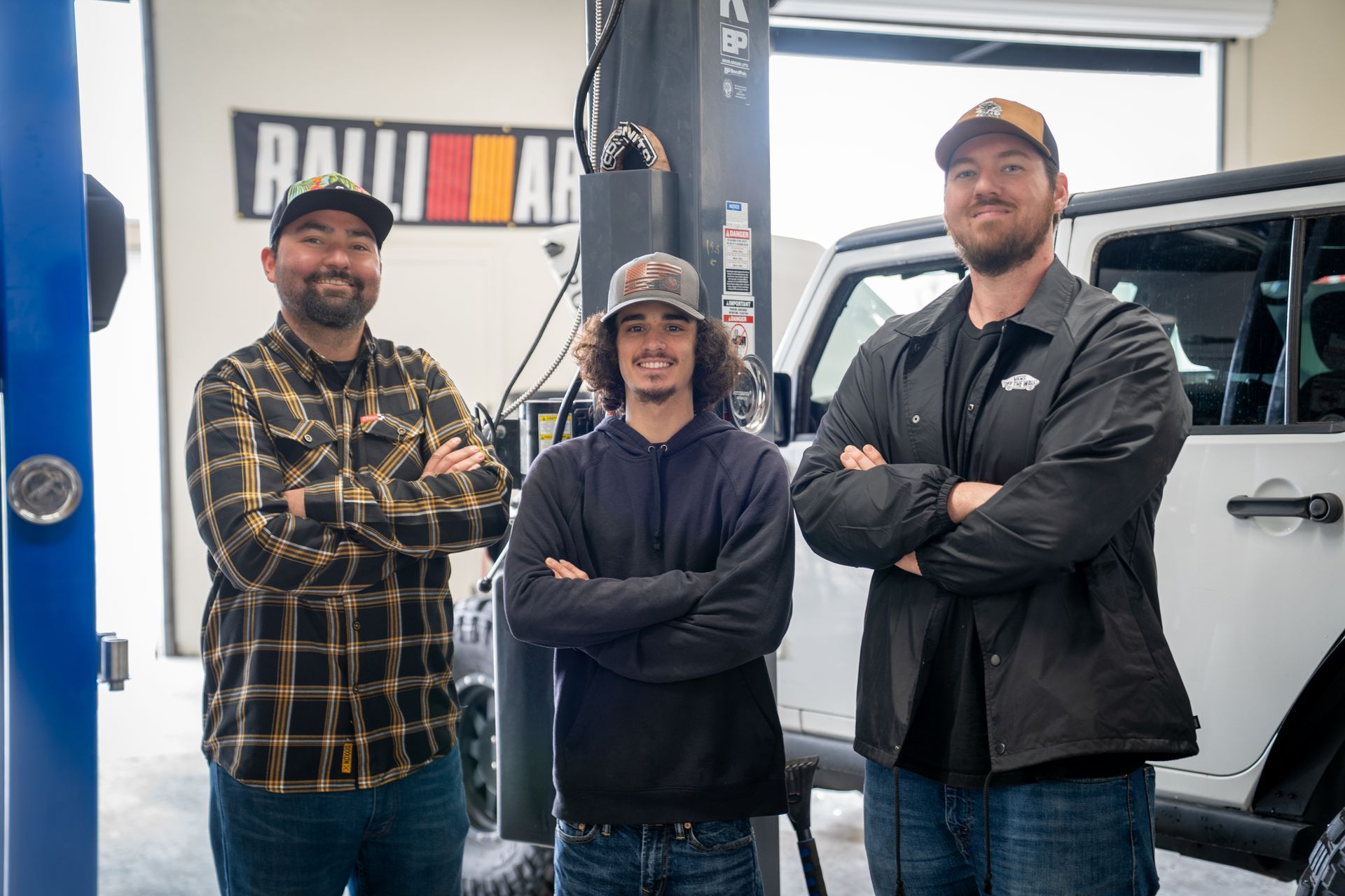 Three men are standing next to each other in a garage with their arms crossed.