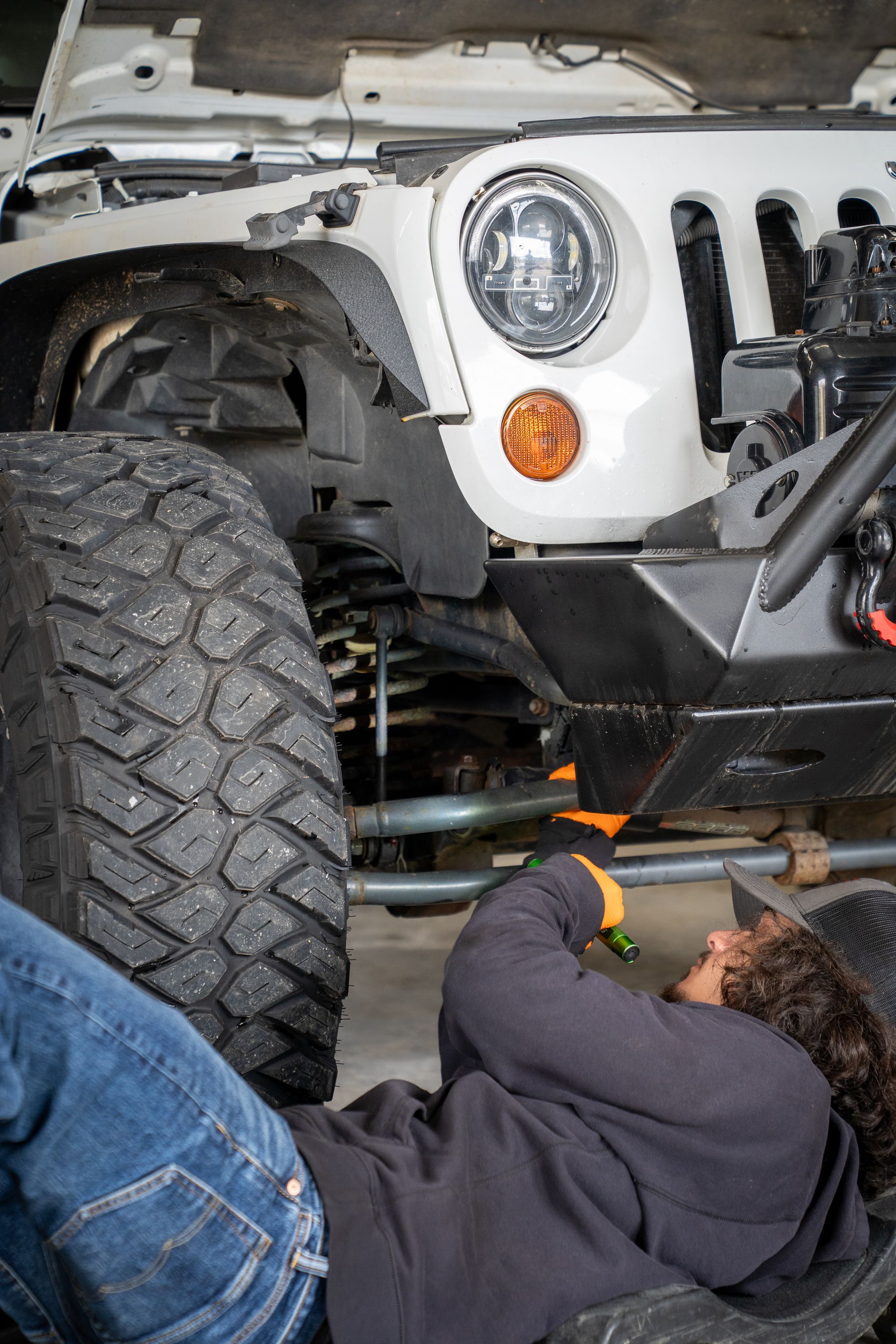 A man is laying on the ground working on a white jeep.