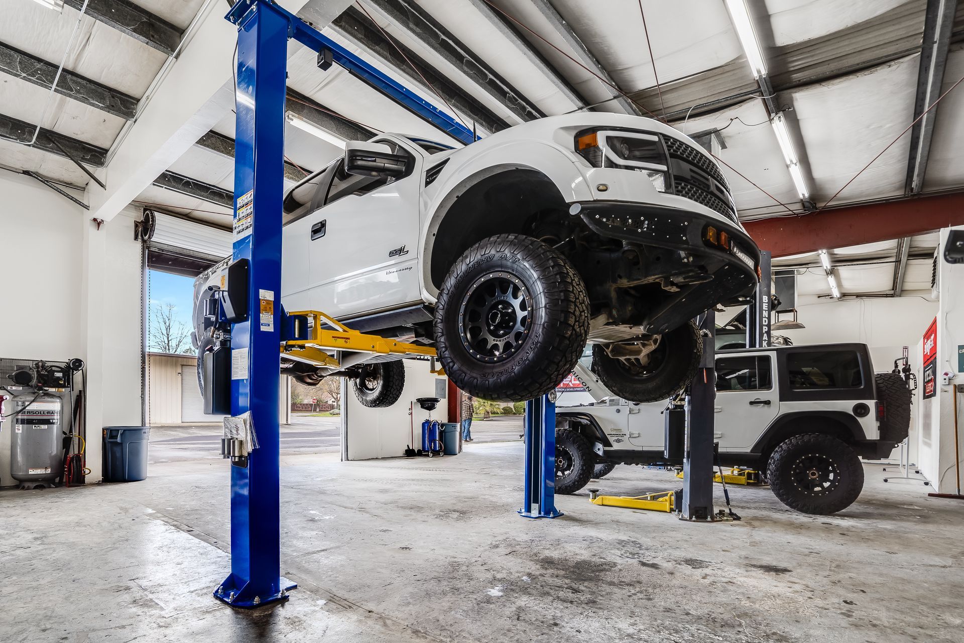 A white truck is sitting on a lift in a garage.
