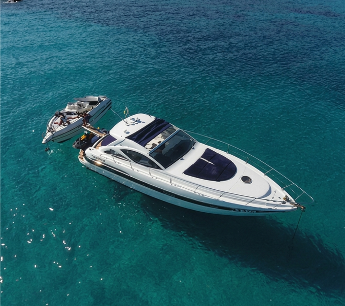 Uno yacht bianco che traina una barca più piccola su acque cristalline color turchese.