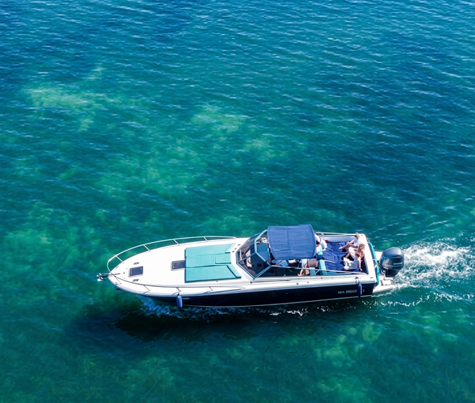 Piccola imbarcazione a motore su acque cristalline con persone a bordo, vista dall'alto.