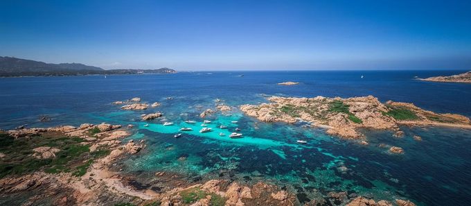 Laguna rocciosa costiera con acque turchesi e piccole imbarcazioni sotto un cielo azzurro limpido.