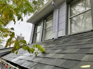 The roof of a house with a gray shingle roof and two windows.