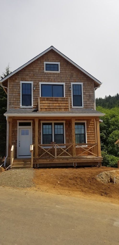 A large house with a porch and a lot of windows is sitting on top of a dirt hill.