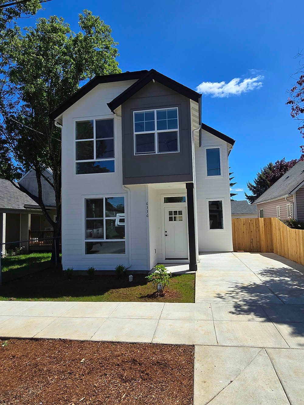 A white house with a gray roof and a lot of windows is for sale.