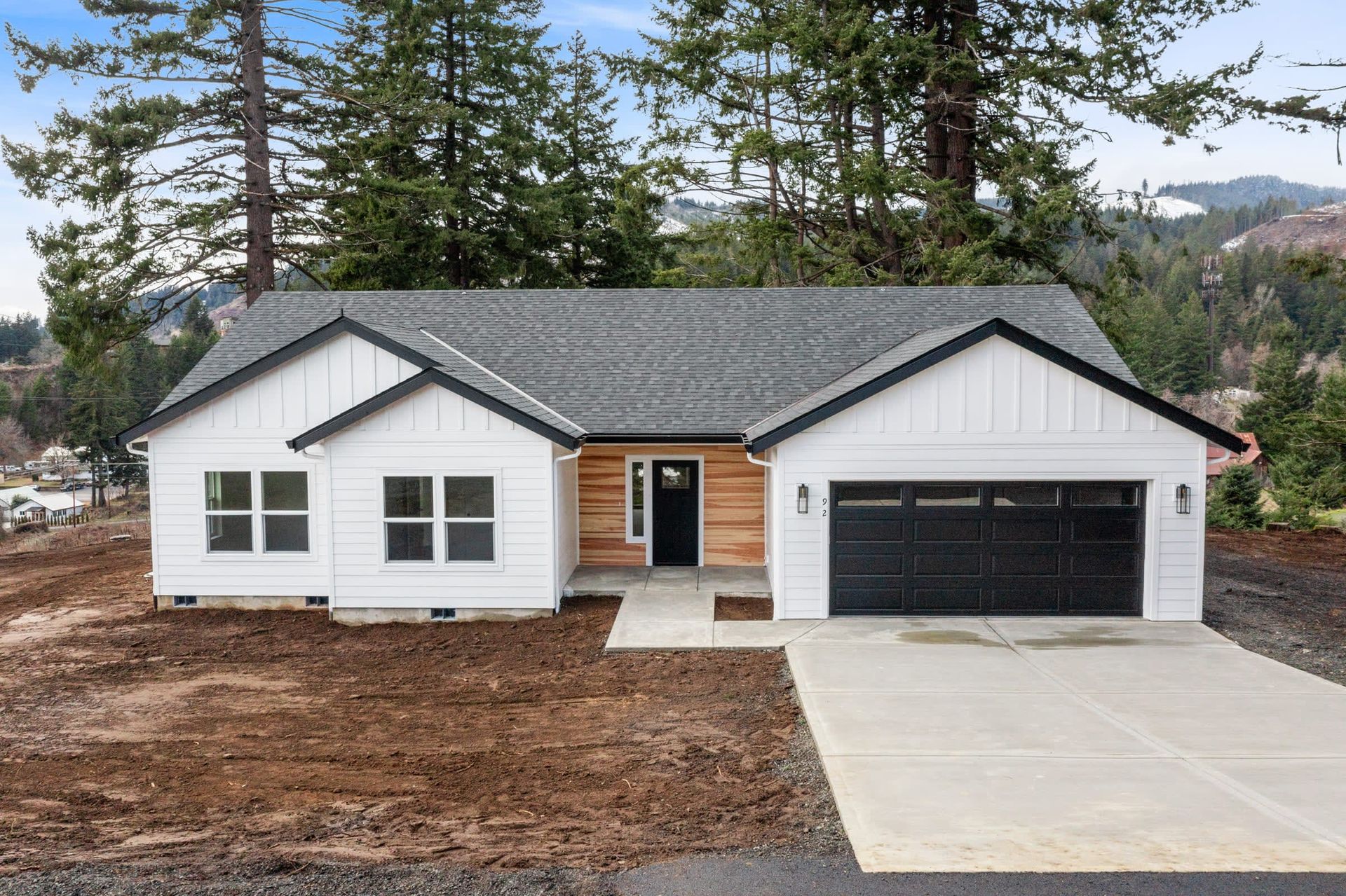 A white house with a black garage door is surrounded by trees.