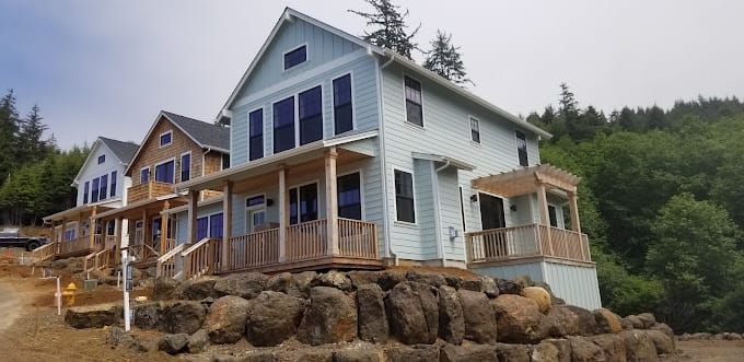 A white house with a black roof is sitting in the middle of a dirt field.