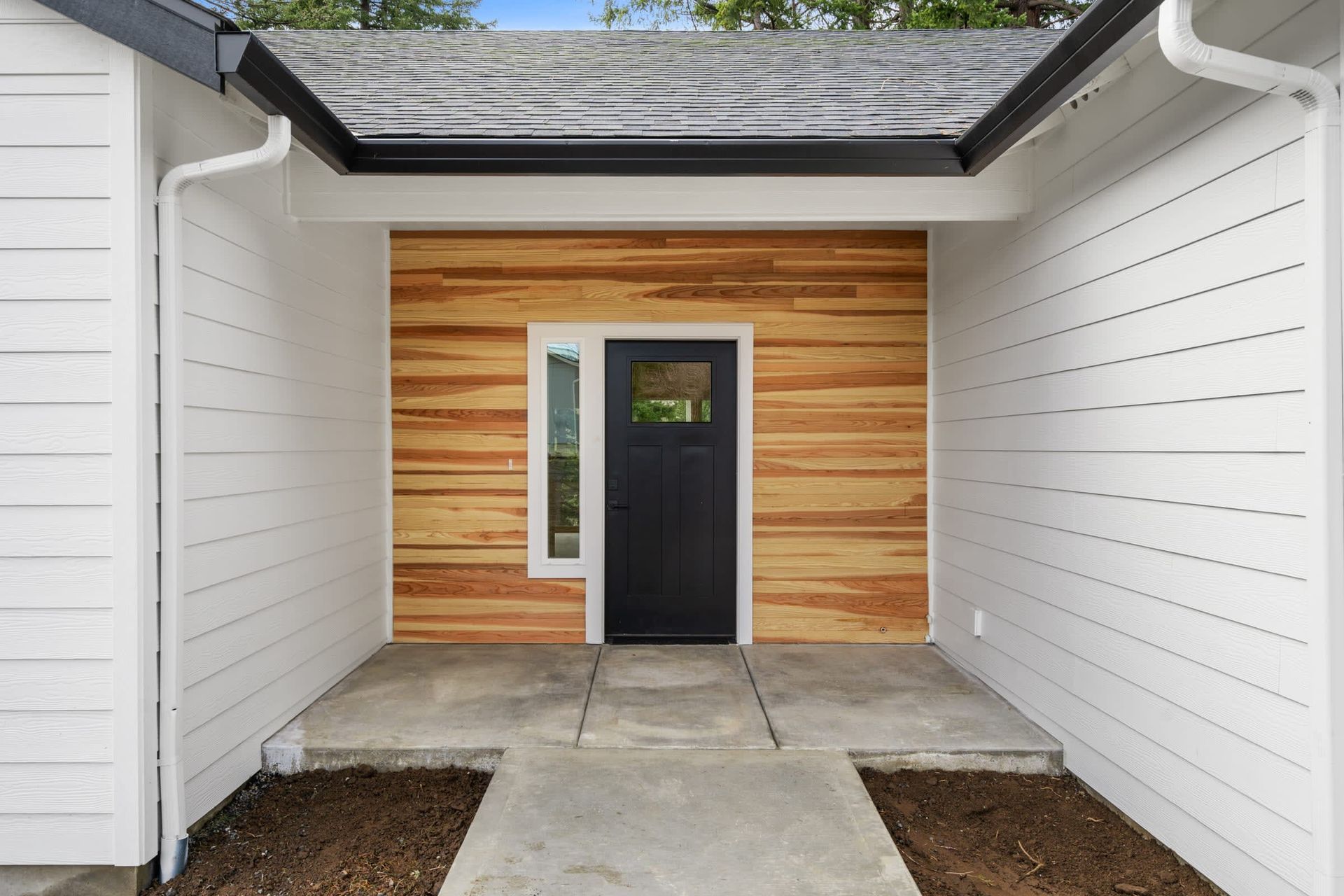 The front door of a house with a black door and wooden siding.
