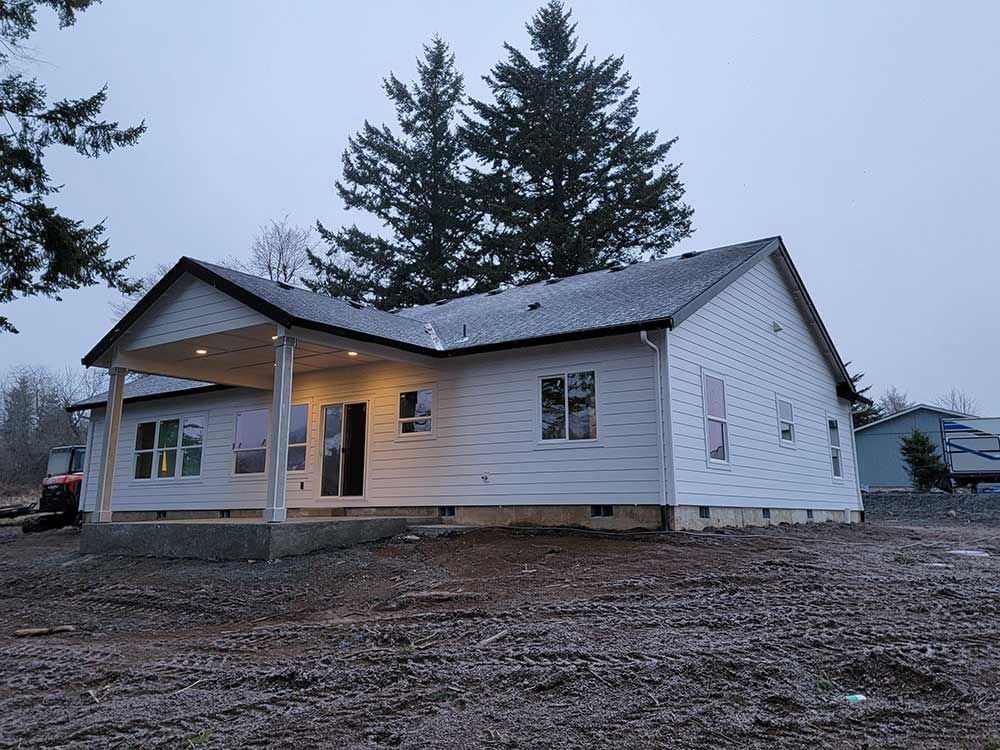 A white house with a black roof is sitting in the middle of a dirt field.