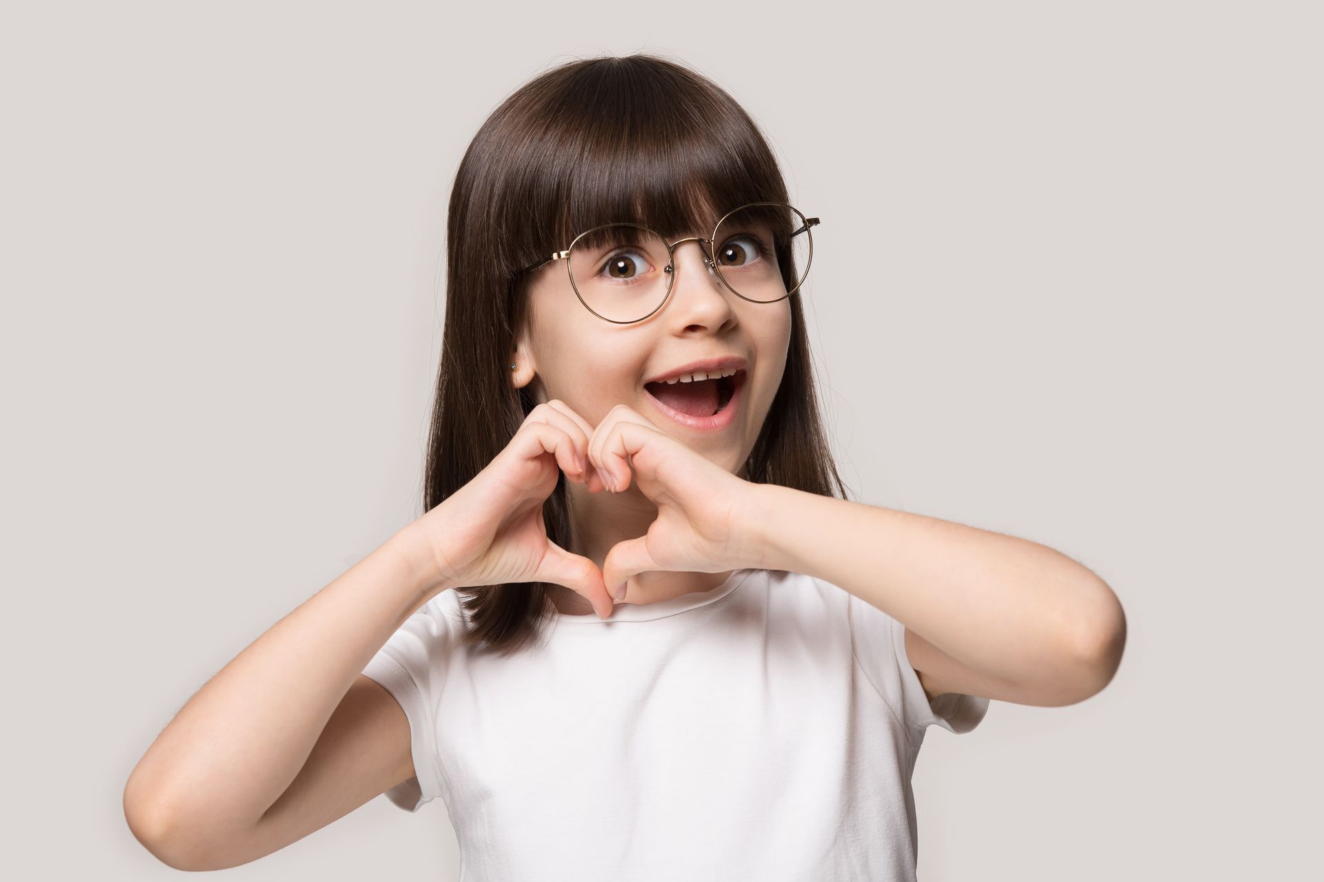 A little girl wearing glasses is making a heart shape with her hands.