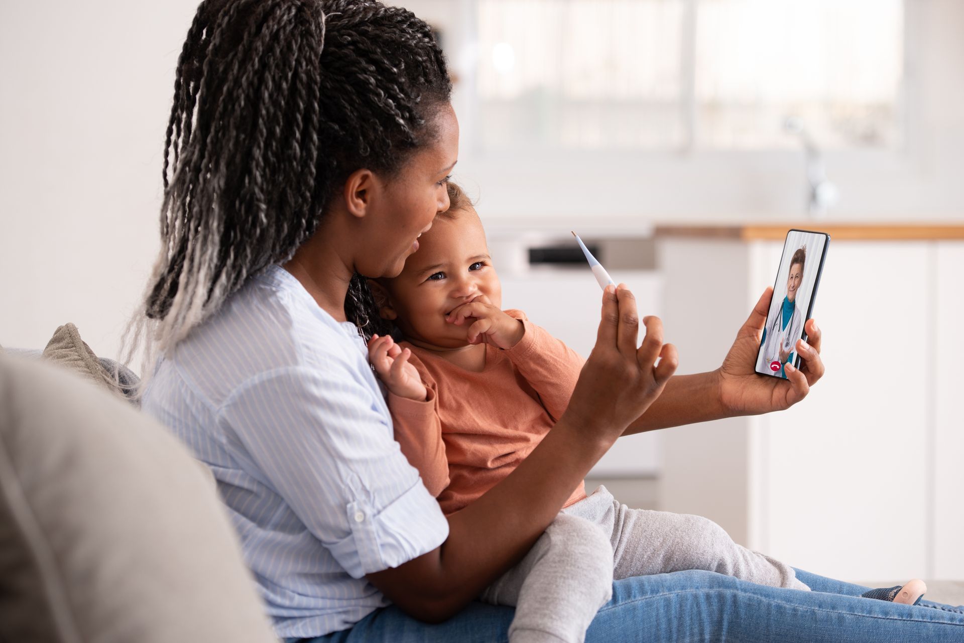 Mother holding her toddler while talking with a doctor on her tablet