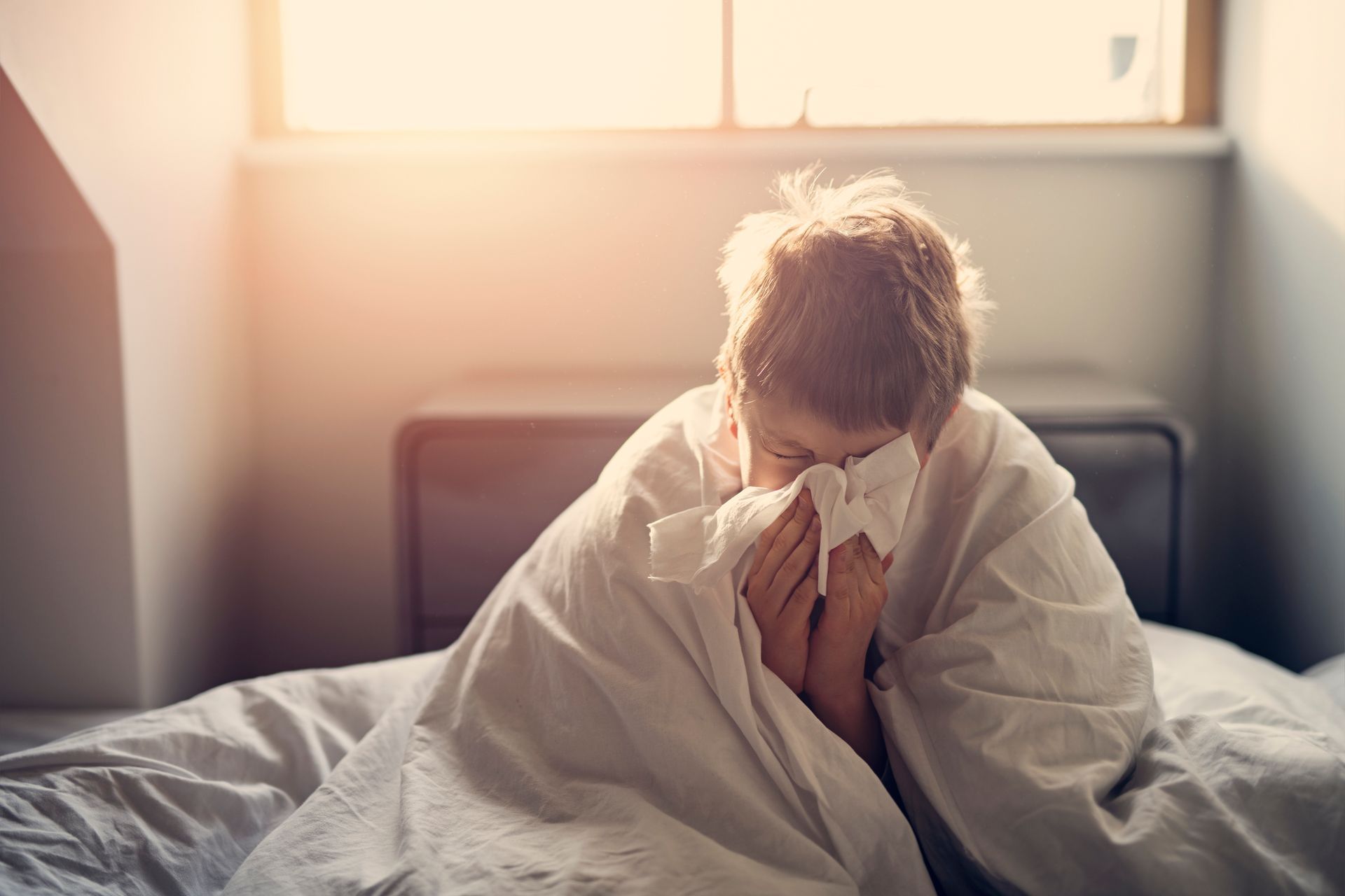 Sick child wrapped in a blanket and blowing their nose