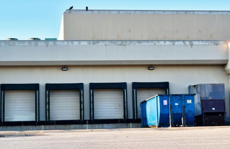 A warehouse with a blue dumpster in front of it.