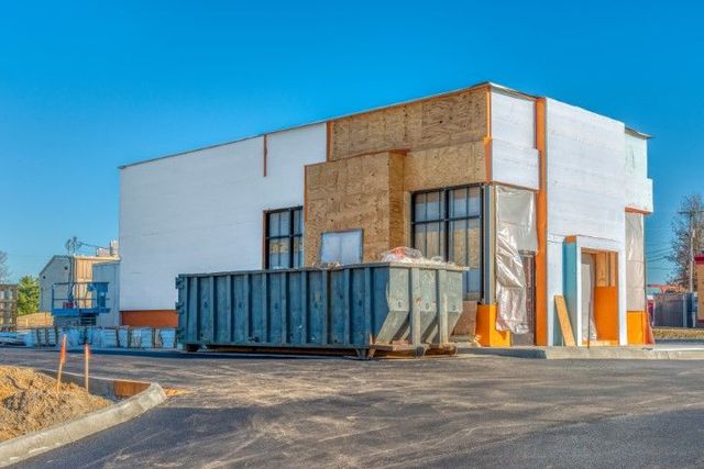 A large dumpster is parked in front of a building under construction.