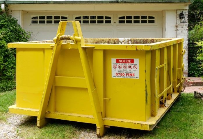 A yellow dumpster is sitting in front of a garage.
