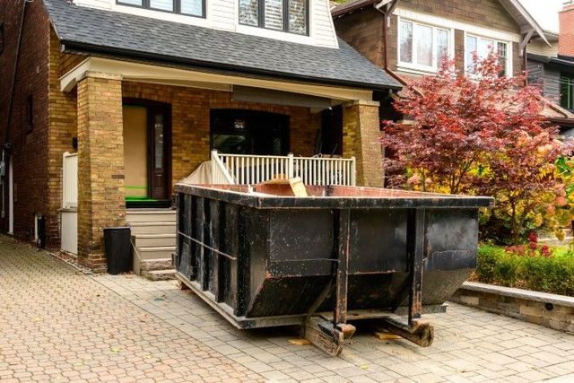 A dumpster is parked in front of a brick house.