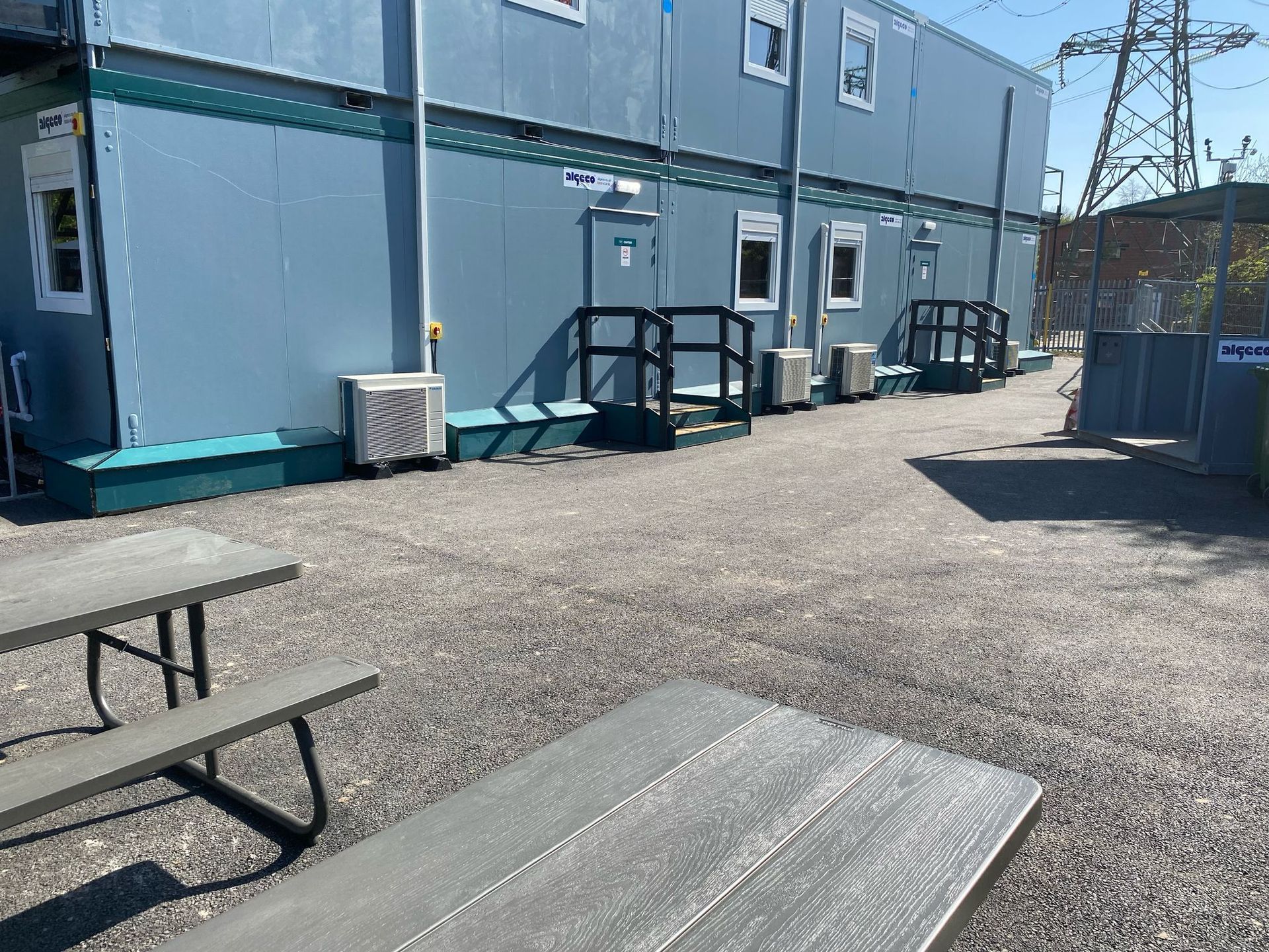 Picnic tables on gravel path in front of a blue modular building.