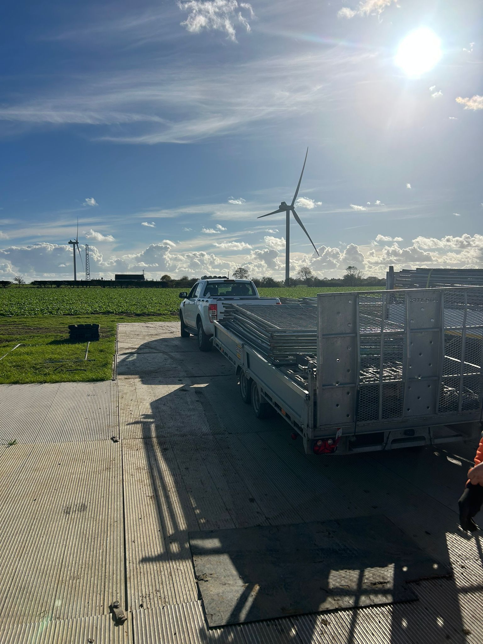 Metal temporary fencing enclosing a grassy area, set along a paved sidewalk in a park.