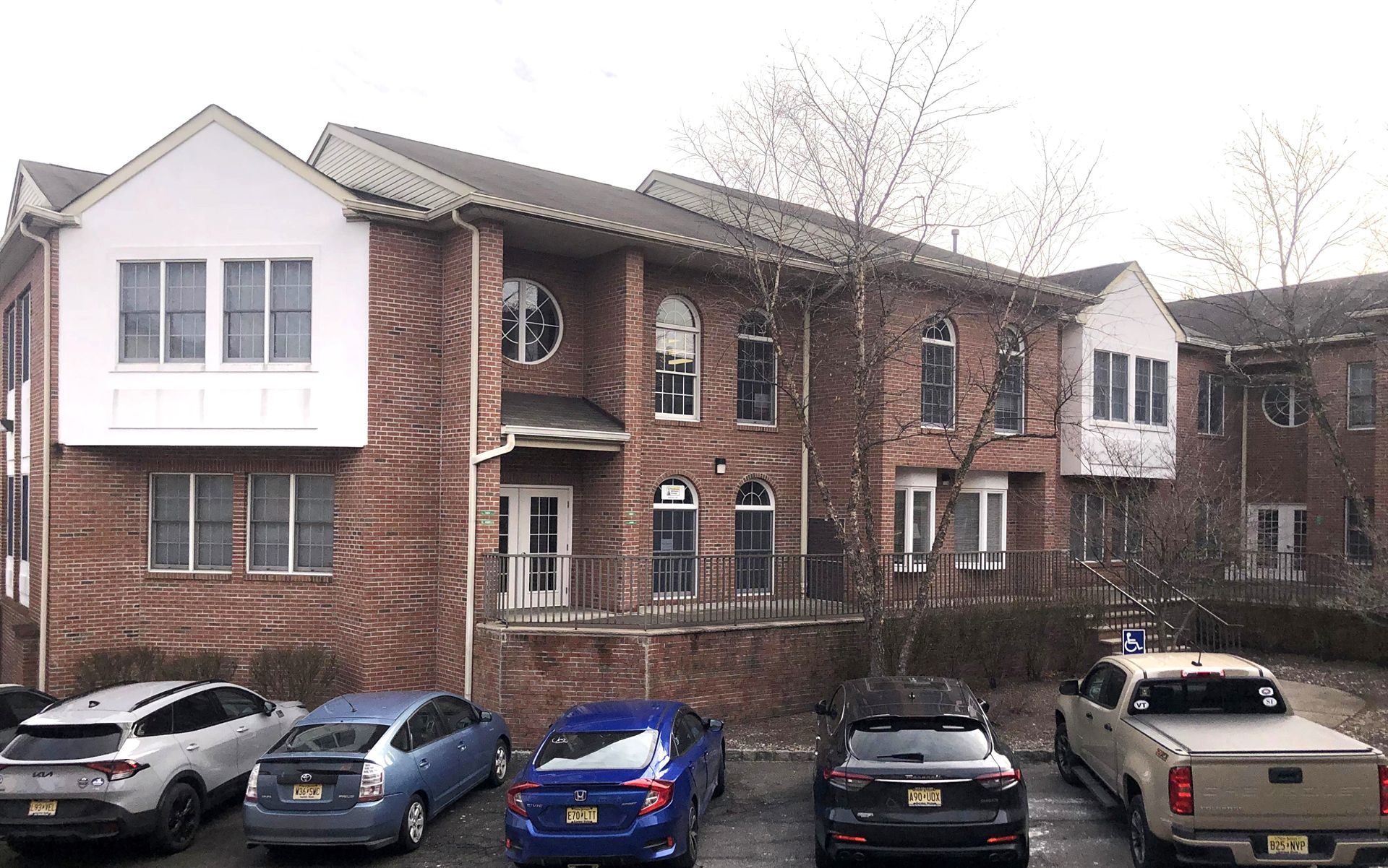 Brick building with multiple windows and a row of parked cars in front.