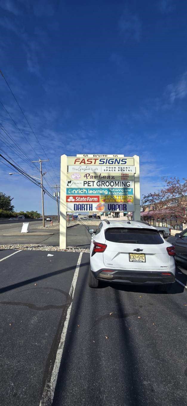 A white car is parked in a parking lot in front of a large sign.