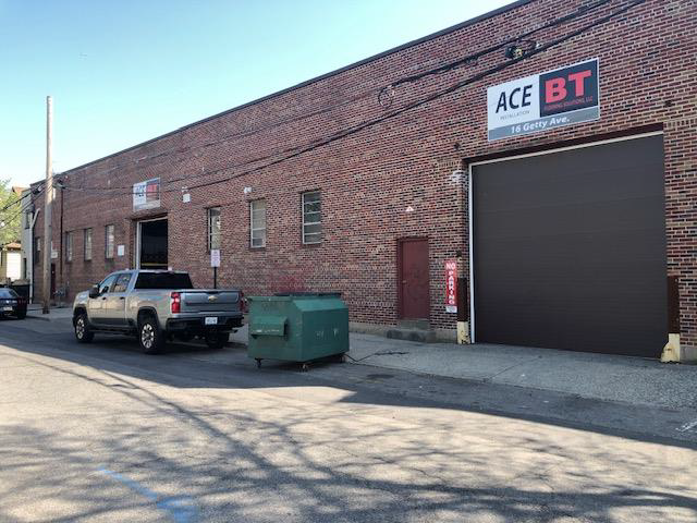 A truck is parked in front of a brick building with a sign that says ace bt.
