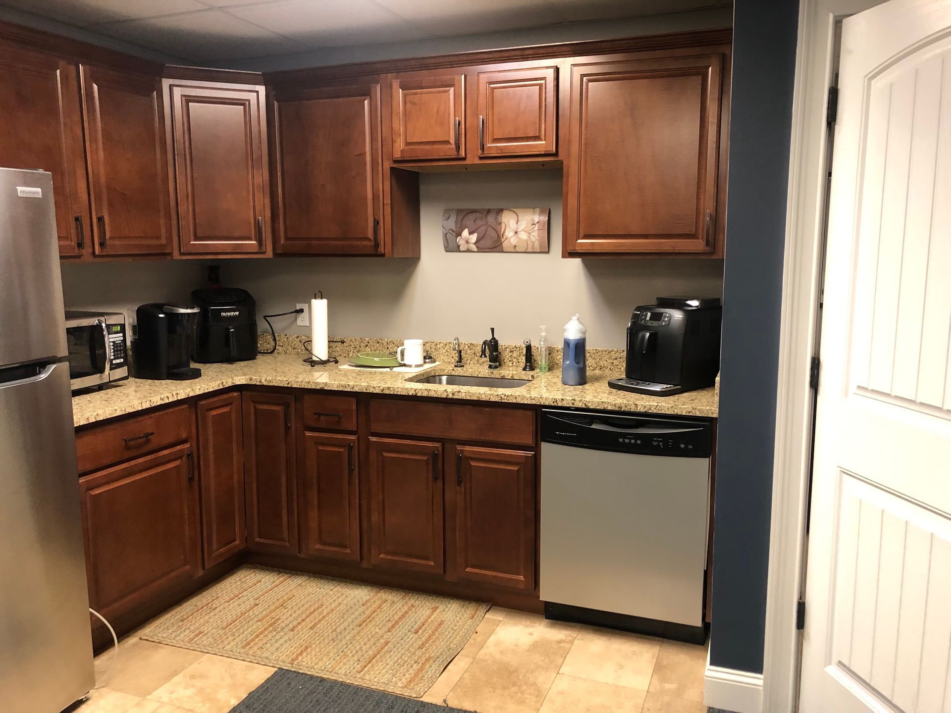 Office kitchenette with brown cabinets, stainless steel appliances, and beige countertops.